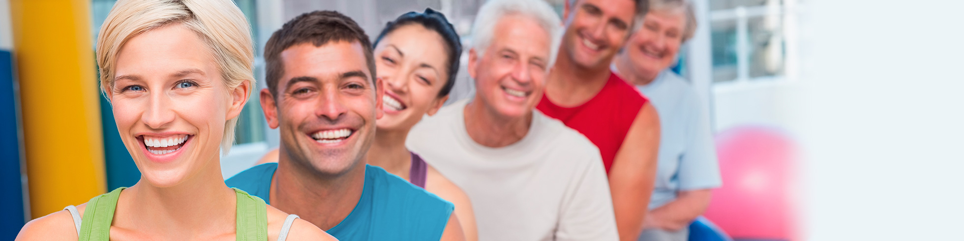 Eine Gruppe strahlender Menschen unterschidlichen Alters und Nationalität im Fitnessraum.